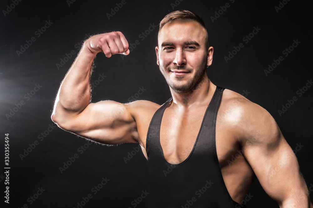 Bodybuilder showing biceps over black background in a black shirt Bodybuilder showing biceps over black background in a black shirt