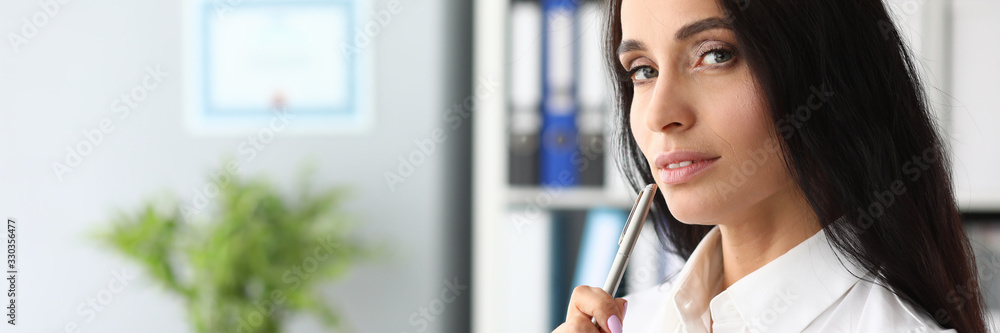 Portrait of joyful woman thinking about something. Smart businesswoman overwhelmed with thoughts standing in modern office and holding paper tablet with pen. Successful entrepreneur job concept