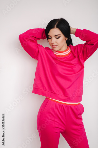 Attractive young model in pink tracksuit. Woman demonstrating clothes in studio. White background © Aleksandr