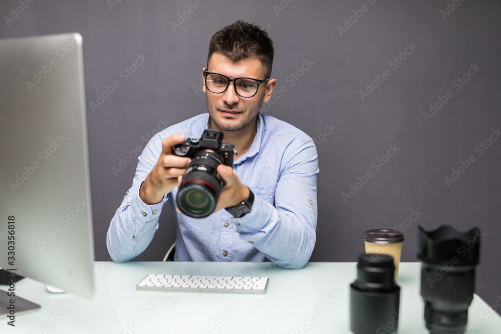 Young man holding digital camera and smiling while sitting at his working place Young man holding digital camera and smiling while sitting at his working place