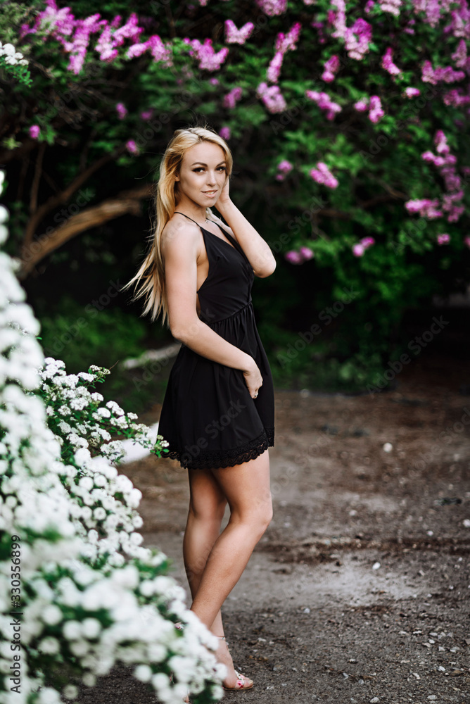 girl in a black dress near the flowers. Blonde woman posing in nature girl in a black dress near the flowers. Blonde woman posing in nature
