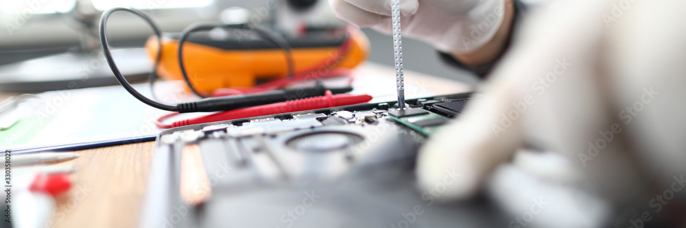 Close-up of technician male hands in gloves using screwdriver to fix laptop parts or install additional memory hardware. Professional repairing gadgets in service center Close-up of technician male hands in gloves using screwdriver to fix laptop parts or install additional memory hardware. Professional repairing gadgets in service center