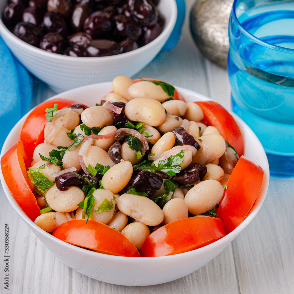 Traditional greek white bean salad with olives in a plate on a business wooden table. Traditional greek white bean salad with olives in a plate on a business wooden table.