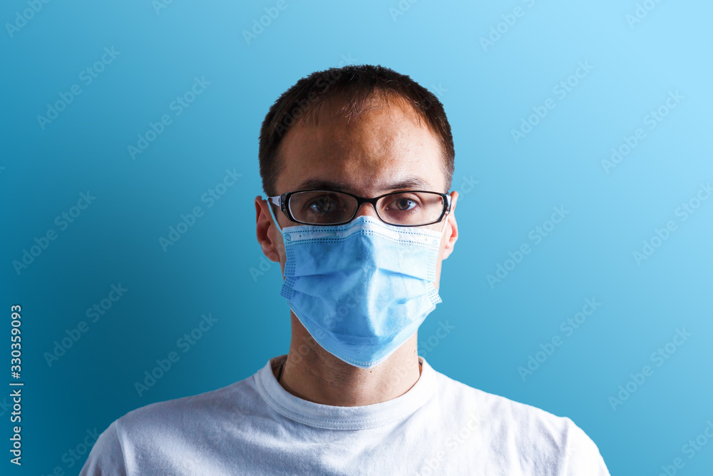 Portrait of a sick man wearing medical mask with coronavirus text at blue background. Coronavirus concept. Protect your health. Portrait of a sick man wearing medical mask with coronavirus text at blue background. Coronavirus concept. Protect your health.