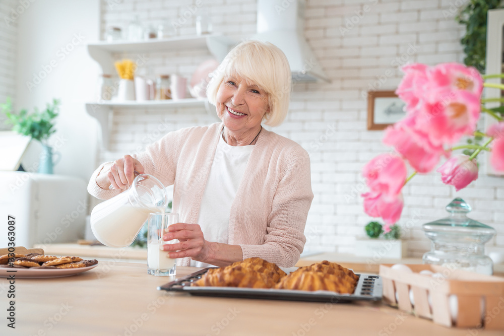Cooking with love. Attractive old woman cooking on kitchen. Cheerful grandmother is baking. Pours milk from a jug Cooking with love. Attractive old woman cooking on kitchen. Cheerful grandmother is baking. Pours milk from a jug