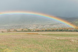 View of a rainbow coming out, in a valley with the mountains in the background.