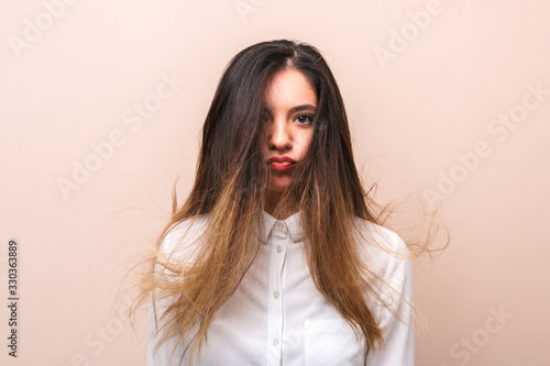 attractive brunette in white shirt with flying hairs makes funny face against pink background. studio shoot