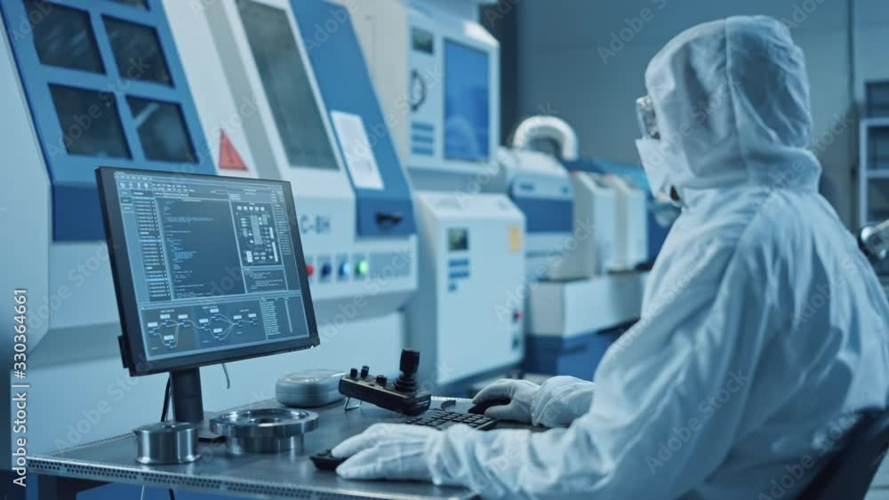 Factory Cleanroom: Engineer Wearing Coveralls Does System Control on a Computer, Uses Controller, Screen Shows Infographics. In Background Modern CNC Machinery, Robot Arm and Electronic Equipment Factory Cleanroom: Engineer Wearing Coveralls Does System Control on a Computer, Uses Controller, Screen Shows Infographics. In Background Modern CNC Machinery, Robot Arm and Electronic Equipment