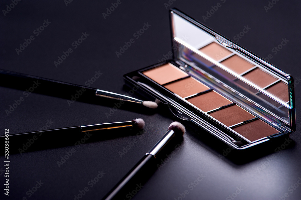 Cosmetic palette and face shadow with brushes lies on a black background Cosmetic palette and face shadow with brushes lies on a black background