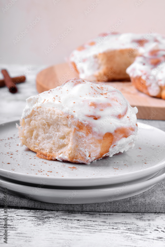 Cinnamon roll topped with cream cheese glazing on the white wooden table Cinnamon roll topped with cream cheese glazing on the white wooden table