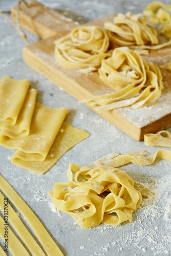 Homemade italian pasta, ravioli, fettuccine, tagliatelle on a wooden board and on a blue background. The cooking process, raw pasta. Tasty raw ravioli with ricotta and spinach,with flour on background