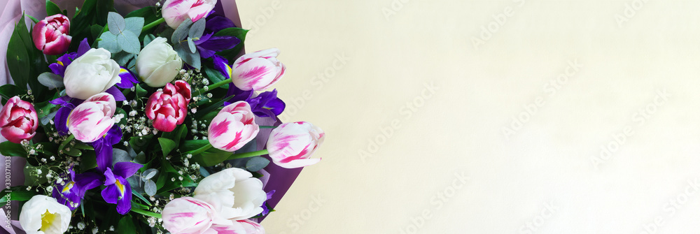 A bright spring bouquet with tulips and irises in a gift box lies on the yellow table A bright spring bouquet with tulips and irises in a gift box lies on the yellow table