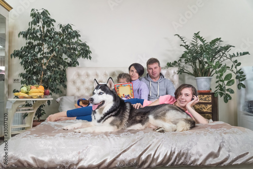 Happy family together with a dog lie on a large bed indoors.