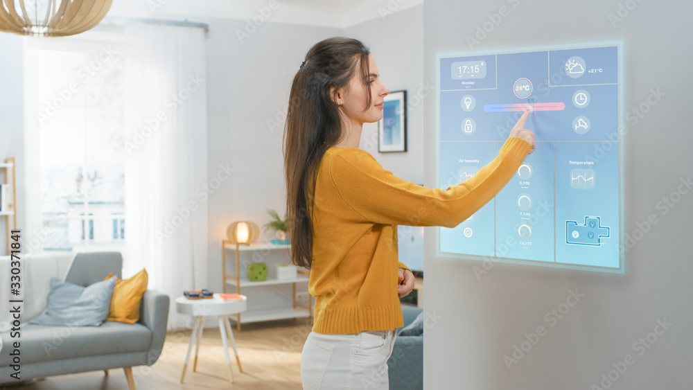Beautiful Young Girl Walks Over to a Refrigerator. She is Changing Temperature on a Smart Fridge Screen at Home. Kitchen is Bright and Cozy. Beautiful Young Girl Walks Over to a Refrigerator. She is Changing Temperature on a Smart Fridge Screen at Home. Kitchen is Bright and Cozy.