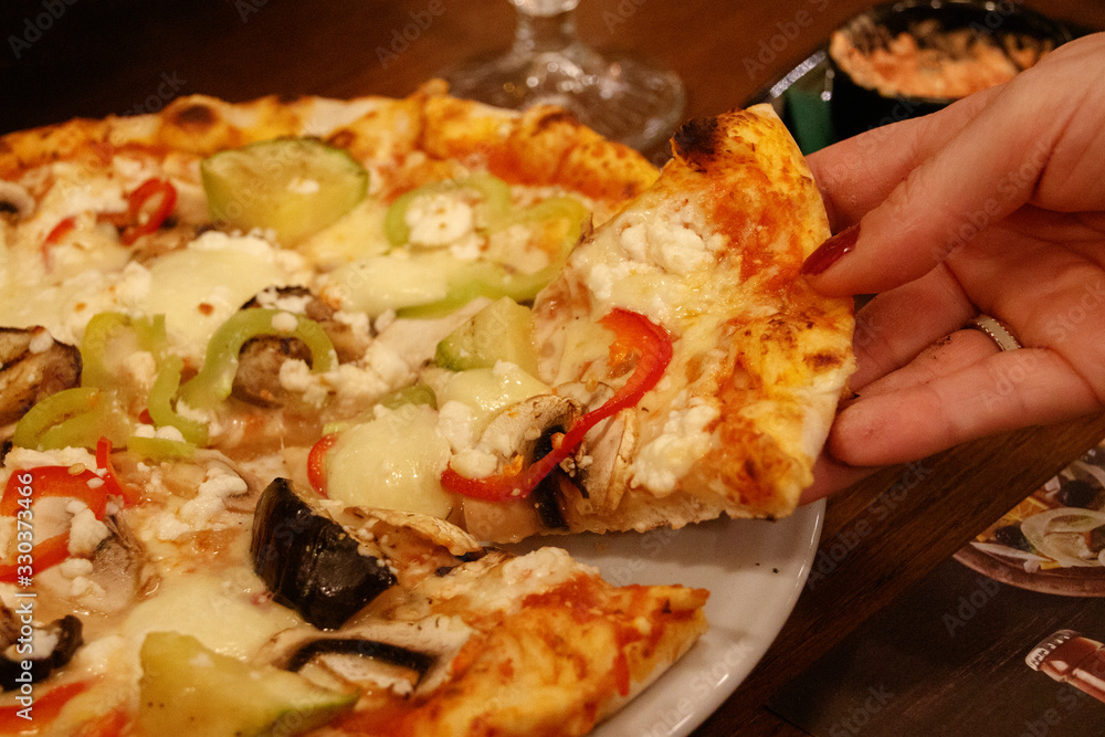 Hand of a woman picking a slice of vegetable pizza