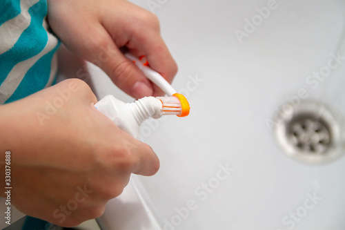 Squeeze toothpaste onto a toothbrush from a tube in the bathroom at home. The child wants to brush his teeth in the morning after eating.