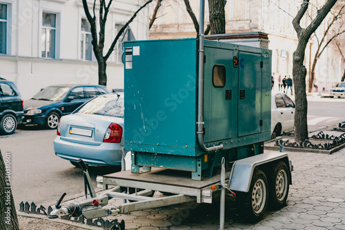 Mobile moveable gensets portable diesel engine power electric generator on a trailer stands on the city's street. Green. Urban. Electricity. Power supplier for business. Outdoor. Sidewalk. Road. Wheel photo