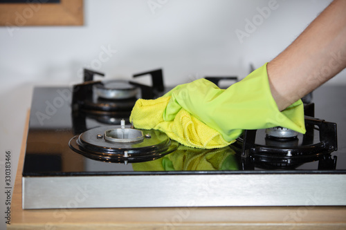 Man hands in rubber green gloves cleaning the gas cooker closeup