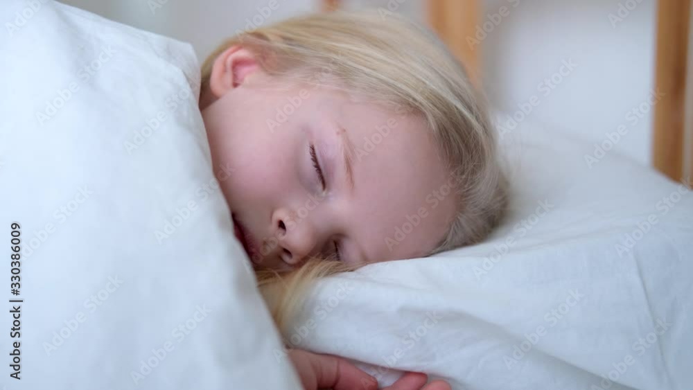 Sleeping little blonde girl close up in big bed with white bedding early in the morning. Children dream. Childhood, calm, night .4k footage Sleeping little blonde girl close up in big bed with white bedding early in the morning. Children dream. Childhood, calm, night .4k footage
