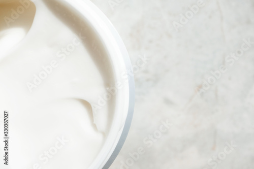 Close-up opening face cream in container on marble background with copy space, top view. Cosmetology detail