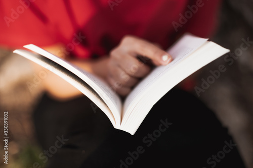 Close up of a open book right in the middle by a young female who is pointing her finger in a word of the page. Low depth of field.