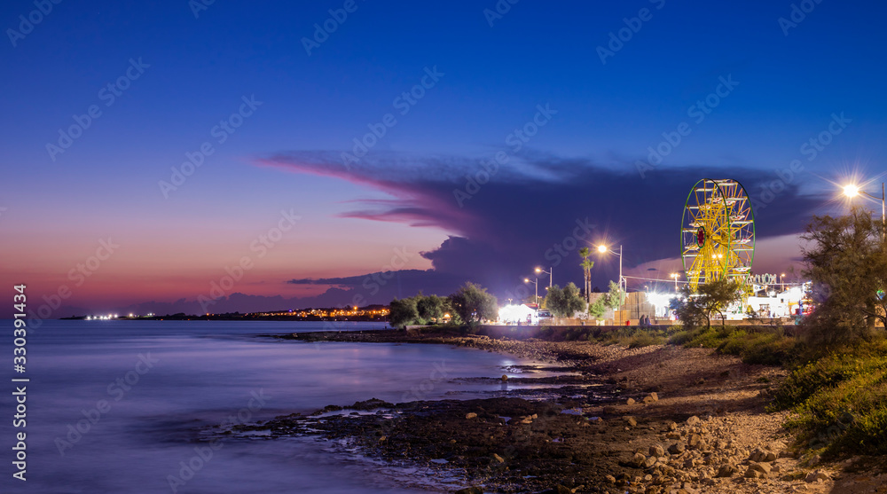 The spectacular panorama of the sea at night, in summer, in Torre Vado. Fun place for tourists, with rides, Ferris wheel, stalls, market, restaurants and fast food. In Italy, Puglia, Lecce, Salento.