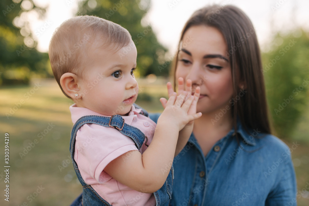 Cute baby on mom's hands outside. Family in the park in summer. Denim style. Mom and daughter in jeans Cute baby on mom's hands outside. Family in the park in summer. Denim style. Mom and daughter in jeans