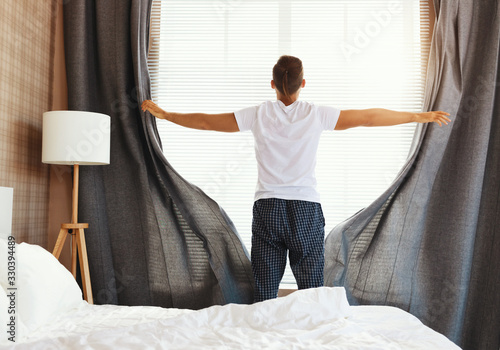 Anonymous man pulling curtains in morning.