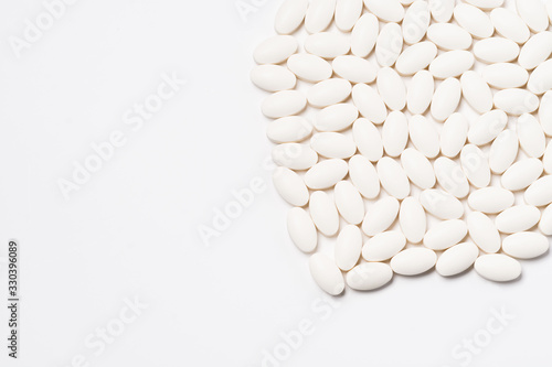 A large number of tablets of white oval-shaped tablets on a white background. View from above