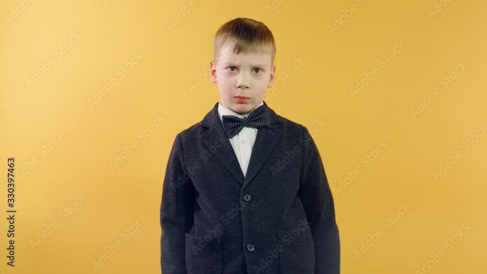 Funny serious boy in black jacket looking at camera standing on yellow background. Sad caucasian boy celebrating birthday alone Funny serious boy in black jacket looking at camera standing on yellow background. Sad caucasian boy celebrating birthday alone
