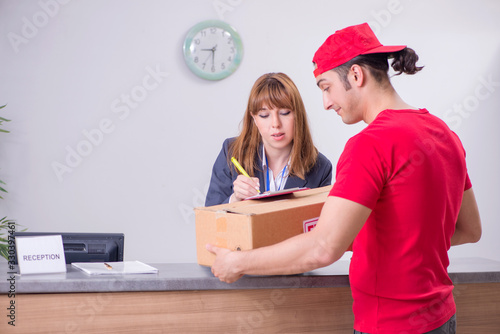 Fotografie Young male courier delivering box to hotel's reception