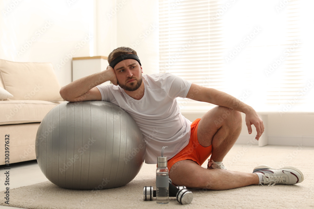 Obraz premium Lazy young man with sport equipment at home