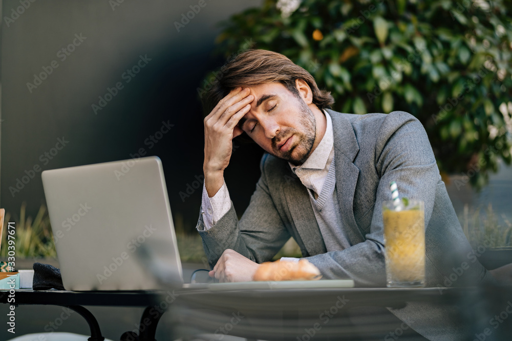 Young businessman having a headache while working on laptop in a cafe, Young businessman having a headache while working on laptop in a cafe,