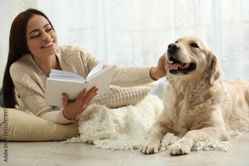 Young woman with book and her Golden Retriever at home. Adorable pet