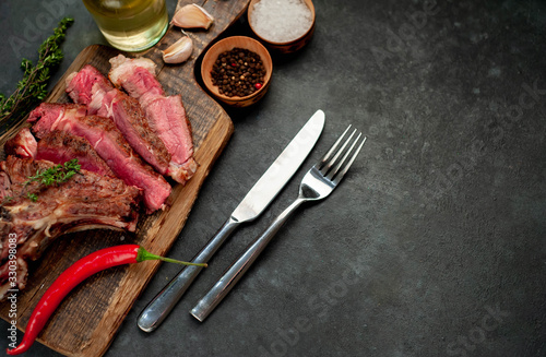 Grilled beef steak with spices and cutlery on a cutting board on a stone background with copy space for your text