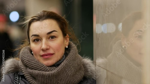 Young pretty lady in office building is standing near polished marble wall in which her face is reflected. Portrait of successful woman in jacket with fur collar in subway. Stream of wind blows hair photo