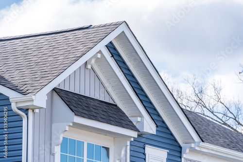 Elegant American house facade, with Shed Roof Over Awning Window, double gable white brackets, gray vertical and blue horizontal vinyl lap siding, white fascia with cloudy blue sky