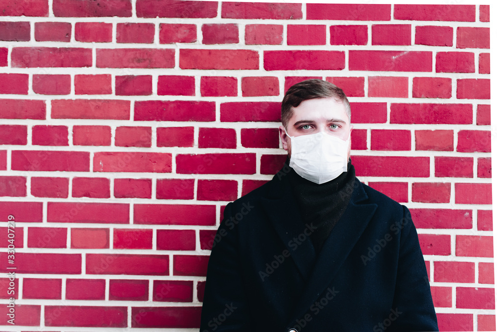 Young caucasian man with surgical mask to protect from coronavirus on a brick wall background with space for text Young caucasian man with surgical mask to protect from coronavirus on a brick wall background with space for text