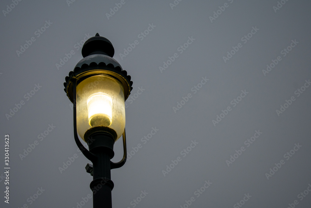 A Turned On Old Fashion Black Metal Light Post on a Dark Gray Sky A Turned On Old Fashion Black Metal Light Post on a Dark Gray Sky