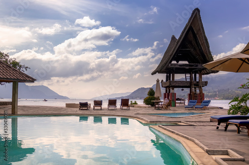 Swimming pool, sun loungers, gazebo in the form of a traditional Indonesian dwelling and a view of the lake, mountains and sky with clouds