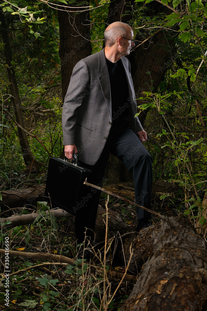 Businessman in jacket with briefcase looking back while lost in a thick forest