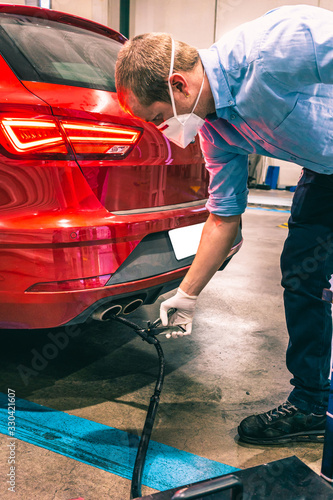 A technician doing an emission control of a security inspection of a vehicle protected with a mask and gloves to prevent the spread of virus