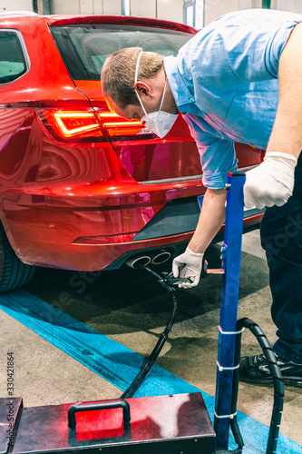 A technician doing an emission control of a security inspection of a vehicle protected with a mask and gloves to prevent the spread of virus