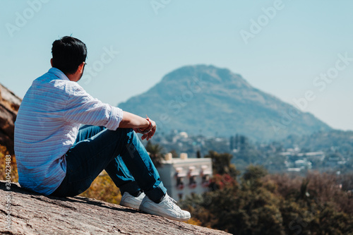 Wallpaper Mural Indian male model staring at the mountain while sitting on rock at Mount Abu in