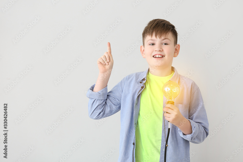 Cute little schoolboy with glowing light bulb on grey background Cute little schoolboy with glowing light bulb on grey background