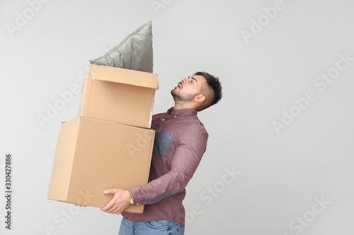 Troubled man with moving boxes on light background