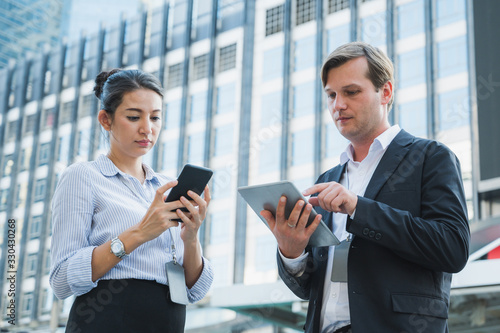 Portrait of businessman and woman using tablet and smartphone while standing on urban city background