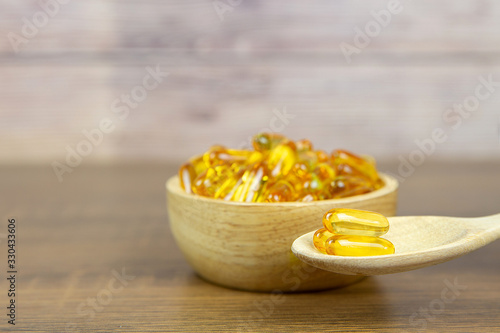 A pile of cod liver oil capsule in a cup and wooden spoon. Dietary supplement for health-care concepts.