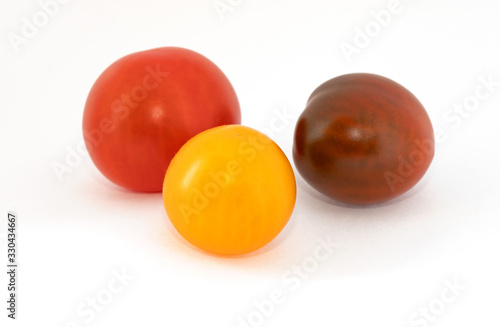 Three multi-colored cherry tomatoes on a white background. Yellow, red, brown