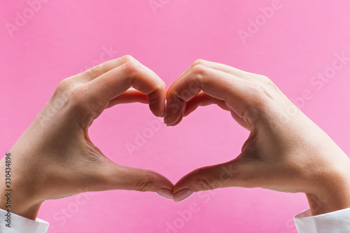 Feminine hands forming a heart symbol on pink background